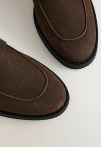 Pair of brown suede loafers with black soles, showing detailed stitching and smooth texture on a light background.
