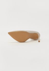 Scarpa con tacco a punta in materiale argento lucido con suola in gomma color sabbia. Presenta un tacco sottile a stiletto e una texture liscia.
