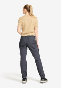 Beige kortärmad skjorta och mörkgrå cargobyxor med fickor och justerbara ärmslut, bärs med vandringsskor. Bakifrån.