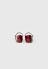 Chaussures plates en cuir verni rouge avec une sangle à l'arrière, texture lisse, bout rond et un petit talon. Design simple avec peu de matériel.