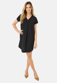 Svart kortärmad klänning med V-ringning och veckdetaljer, tillverkad av mjukt tyg. Sömmen är något rundad, vilket framhäver silhuetten.