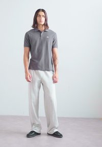 Graues Poloshirt mit kurzen Ärmeln, kombiniert mit hellgrauen Sweatpants. Flache Schuhe mit schwarzen Akzenten. Einfaches, lässiges Design und lockere Passform.