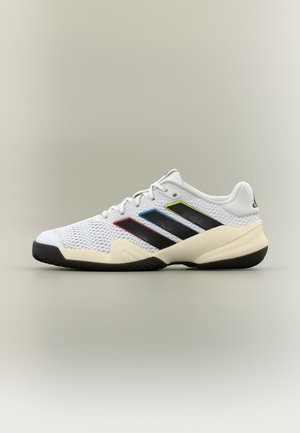 Witte sportschoen met zwarte zool, bovenwerk van mesh en drie zwarte strepen op de zijkant, omlijnd in rood, blauw en geel.