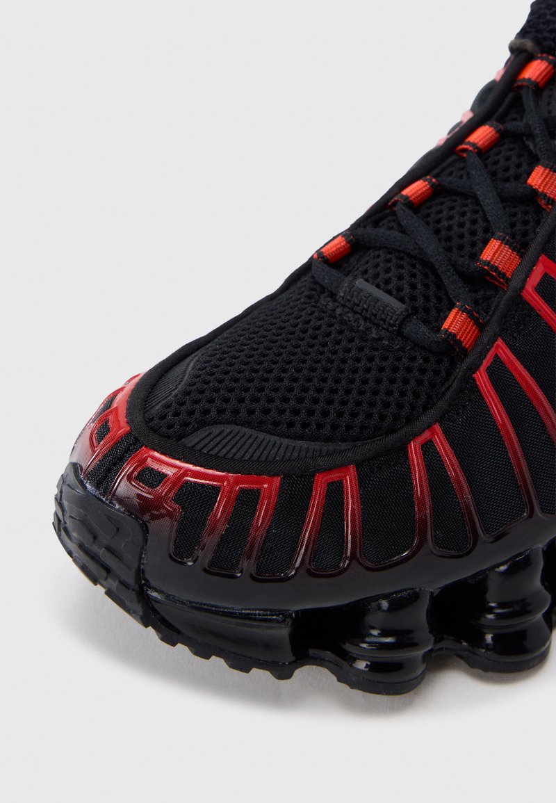 Black athletic shoe featuring a mesh upper, red accents, and a distinct curved sole design with visible cushioning elements.