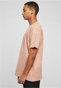 Lyserød bomulds t-shirt, rund halsudskæring, korteærmer, afslappet pasform, sideprofil, glat tekstur, ensartet design uden mønstre eller detaljer.