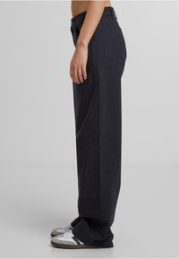 Pantalones de tiro alto y pierna ancha en tejido de color azul marino oscuro, con bolsillos laterales y un bolsillo trasero, combinados con zapatillas blancas y grises.