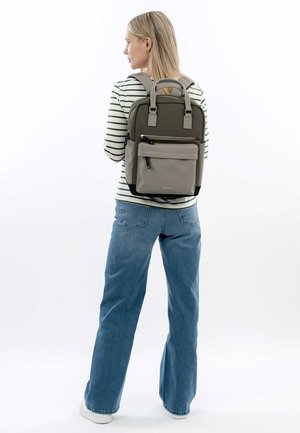 Zaino grigio e verde con spallacci imbottiti, tasca frontale con zip, dettagli in tessuto e un design strutturato. Parte superiore a righe e jeans blu visibili.
