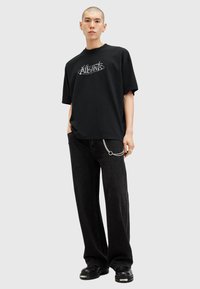 Sort oversized T-shirt med et grafisk logo på fronten. Parret med løstsiddende sorte jeans og kraftige sorte sko. Sølv kædedetalje på jeansene.