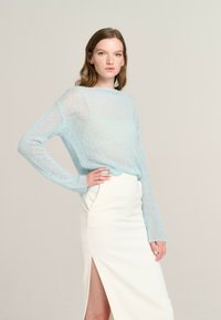 Light blue knitted sweater with long sleeves, semi-sheer texture. Paired with a white skirt featuring a thigh-high slit. Simple, modern design.