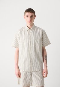 Short-sleeved cream shirt featuring vertical navy stripes, a front pocket, and classic button-up design. Paired with matching shorts.