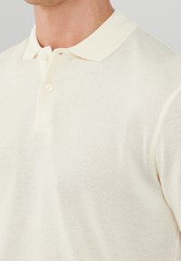 Krämfärgad polo skjorta med strukturerad, andningsbar stickad tyg, med klassisk krage och knappslå med två knappar.