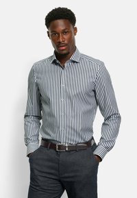Blauw-wit gestreepte overhemddress met een button-down kraag en een getailleerd silhouet, gecombineerd met donkere broeken en een leren riem in het bruin.