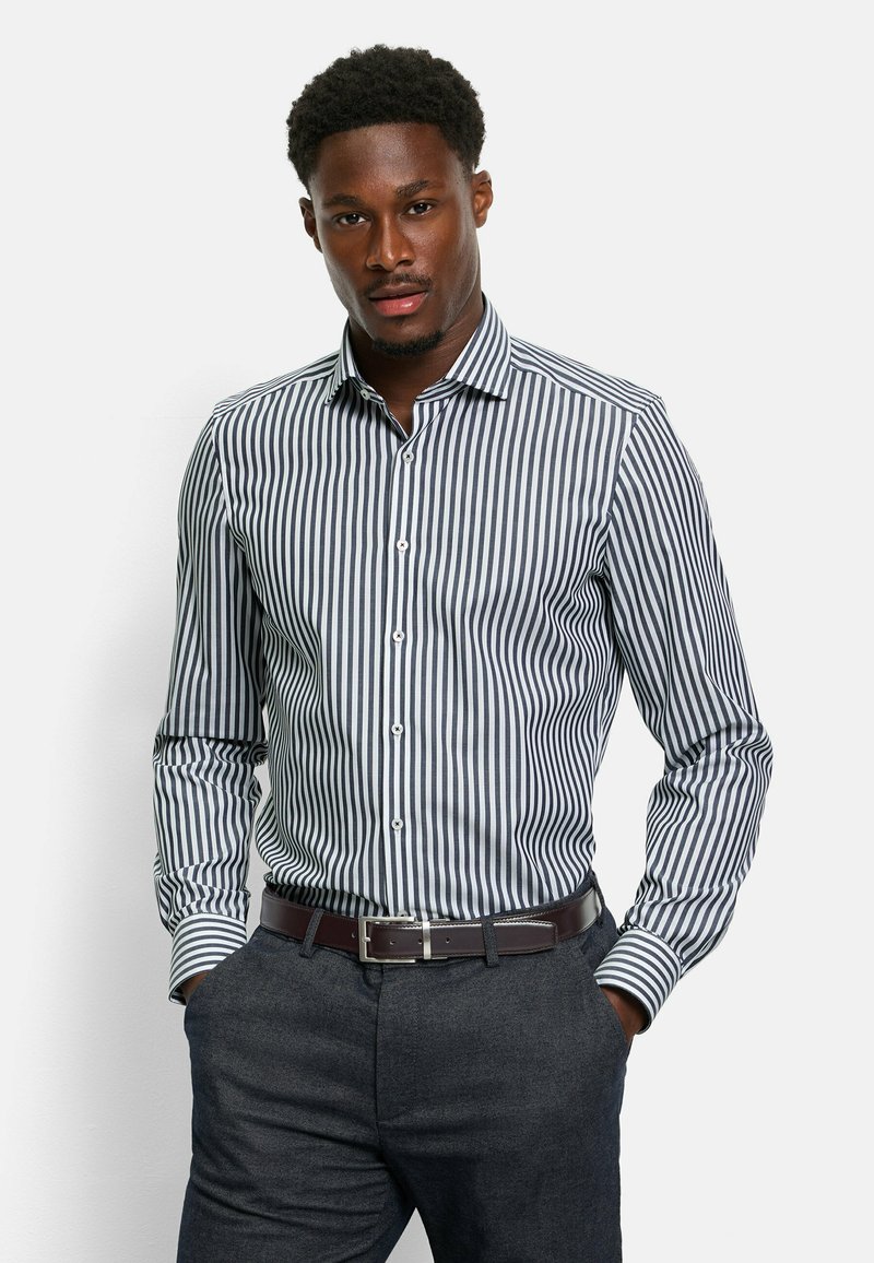 Blauw-wit gestreepte overhemddress met een button-down kraag en een getailleerd silhouet, gecombineerd met donkere broeken en een leren riem in het bruin.