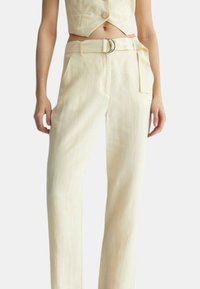 Pantaloni in lino crema con taglio dritto, dotati di una cintura con fibbia argentata, tasche laterali e una texture liscia.