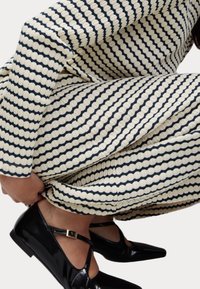 Robe tricotée en crème et bleu marine avec des rayures ondulées ; tissu texturé ; associée à des ballerines en cuir verni noir avec une bride de cheville et un bout pointu.