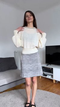 Světlý krémový svetr s balonovými rukávy a ozdobným výstřihem, kombinovaný se sukní se vzorem jezevčíka v šedé a černé barvě a černými balerínkami.