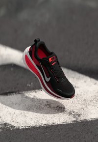 Chaussure de course noire et rouge avec un dessus en maille, un motif texturé, une semelle rembourrée et un logo swoosh blanc. Flottant au-dessus d'une ligne de piste peinte.