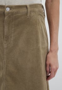 Khaki corduroy skirt featuring vertical ribbing, a button closure, and side pockets. The fabric has a soft, textured appearance.