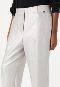 Pantalons ajustés argentés et brillants avec une texture lisse, des plis simples et un accent logo subtil près de la taille.