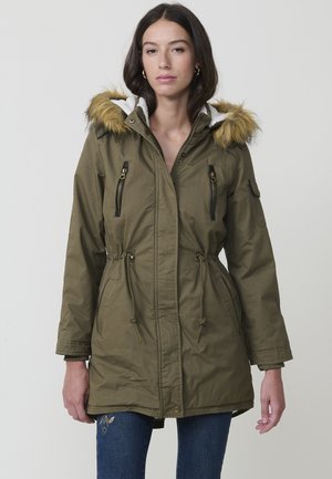Parka de color verde oliva con capucha de piel sintética, bolsillos con cremallera, cintura con cordón y un suave forro interior, con un diseño de puños elásticos.