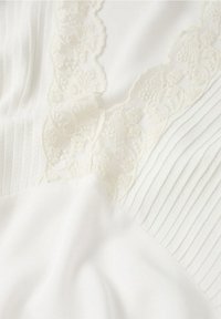Hvid bluse med tekstureret plissering, indviklet blondekant og glat stof. Har bløde draperinger og en kombination af mønstre.