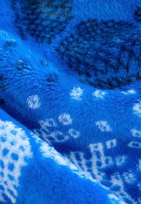 Pătură din fleece de un albastru vibrant cu accente albe modelate. Textură moale, cu diferite forme și designuri, creând un aspect confortabil.