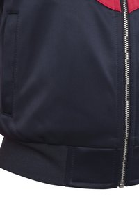 Marine bomberjakke med røde detaljer, teksturert stoff, sølvglidelås og ribbestrikket midje. Har sidelommer og et sporty design.