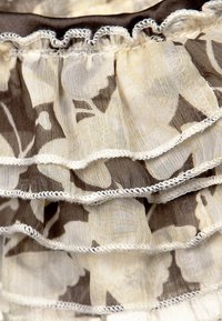 Marszczony materiał z kwiatowymi wzorami w kolorze kremowym i brązowym, z delikatnym białym wykończeniem wzdłuż brzegów. Miękka, lekka tkanina.