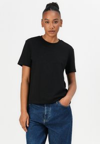 Svart bomulls T-skjorte med korte ermer og rund hals, med subtil "Calvin Klein" branding i midten. Båret med blå jeans.