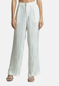 Pantalons blancs à plis, larges, en tissu léger avec un motif texturé subtil, associés à des sandales à talons argentées.