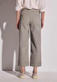 Hellgraue, cropped Hose mit glatter Textur, elastischem Bund und zwei Gesäßtaschen. Kombiniert mit Sneakers mit goldenen Akzenten.