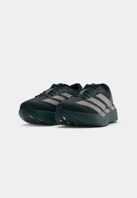Chaussures de sport vert foncé avec des rayures grises, tige en mesh et col rembourré. Semelle épaisse avec des découpes pour la ventilation et le confort.