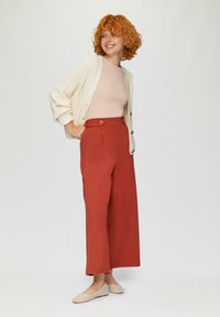 Rode wijde broek met plooien aan de voorkant, knoopsluiting, gecombineerd met een lichtroze geribd topje en een crèmekleurige cardigan. Lichtgeweven instapschoenen.