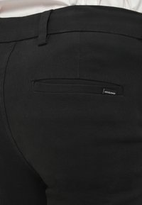 Pantalon noir à texture lisse, doté d'une poche arrière plate et d'une petite étiquette de marque. Design sur mesure avec une coupe épurée.