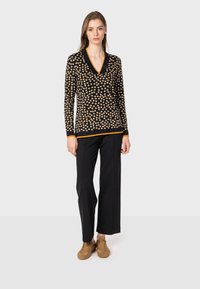 Maglione nero con pois beige, scollo a V, maniche lunghe, rifinito con bordi arancioni. Abbinato a pantaloni neri a gamba larga e scarpe marroni.