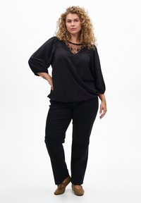 Melna blūze ar teksturētu audumu, caurspīdīgu mežģīņu apkakli un izšuvumiem. Saskaņota ar melniem biksēm un brūniem kurpēm bez stingriem aizdariem.