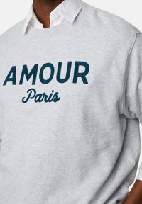 Grijze sweatshirt van zachte katoen met opvallende, marineblauwe geborduurde tekst "AMOUR Paris" in verschillende lettertypen.