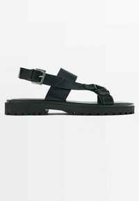 Sandales en cuir noir avec une semelle épaisse et texturée, dotées de sangles ajustables et d'un accent de boucle pour un ajustement sécurisé. Design plat.