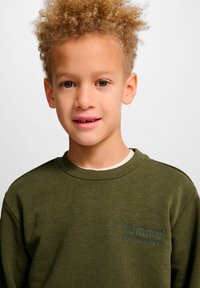 Olivgrüner Pullover mit Rundhalsausschnitt und weicher Textur. Verfügt über einen erhabenen Logodruck auf der linken Brust. Einfaches, lässiges Design.