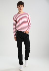 Maglietta a maniche lunghe a righe rosse e bianche abbinata a pantaloni neri e sneakers bianche. Design semplice, texture liscia e silhouette aderente.