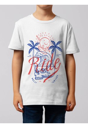 Kind trägt ein weißes T-Shirt mit einer Grafik einer lächelnden Sonne, die auf der Welle surft, über einem Totenschädel, umgeben von zwei Palmen und rotem "Ride"-Text.