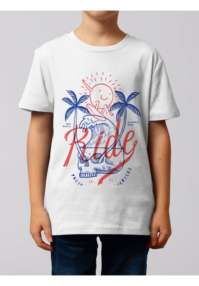 Enfant portant un t-shirt blanc avec un motif de soleil souriant surfant sur une vague au-dessus d'un crâne, encadré par deux palmiers et le texte rouge « Ride ».