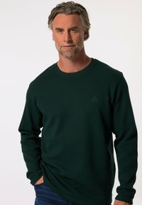 Camicia a maniche lunghe verde scuro con un motivo a nido d'ape testurizzato e scollatura rotonda. Presenta un piccolo logo sul petto.
