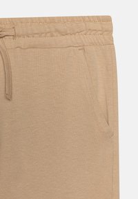 Pantalons de survêtement beige avec taille à cordon, texture douce, poches latérales et coupe slim. Fabriqués en tissu léger avec une finition lisse.