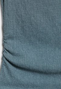 Tessuto grigio-blu con trama, con una cucitura arricciata sul lato sinistro, che mostra una superficie leggermente spiegazzata.