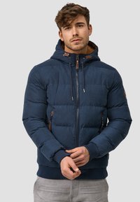 Veste matelassée bleu marine avec capuche, fermeture éclair à l'avant et accents en cuir. Présente des poignets et un ourlet côtelés, deux poches latérales et une texture matelassée.