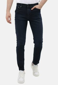 Donkerblauwe slim-fit jeans van denim, met vijf zakken, subtiele wassing, een tailleband met riemlussen, en gecombineerd met witte sneakers.
