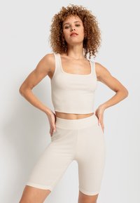 Beige ribbat kort topp med fyrkantig halsringning och matchande högmidjade cykelshorts. Stretchigt tyg och slät textur.