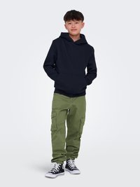 Felpa navy, pantaloni cargo oliva con tasche laterali e sneakers nere alte. La felpa ha un cordino e una tasca frontale.