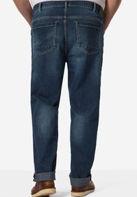 Jeans de denim azul oscuro con corte recto, que cuentan con dos bolsillos traseros y dobladillos enrollados. La textura parece suave con un sutil desgaste.